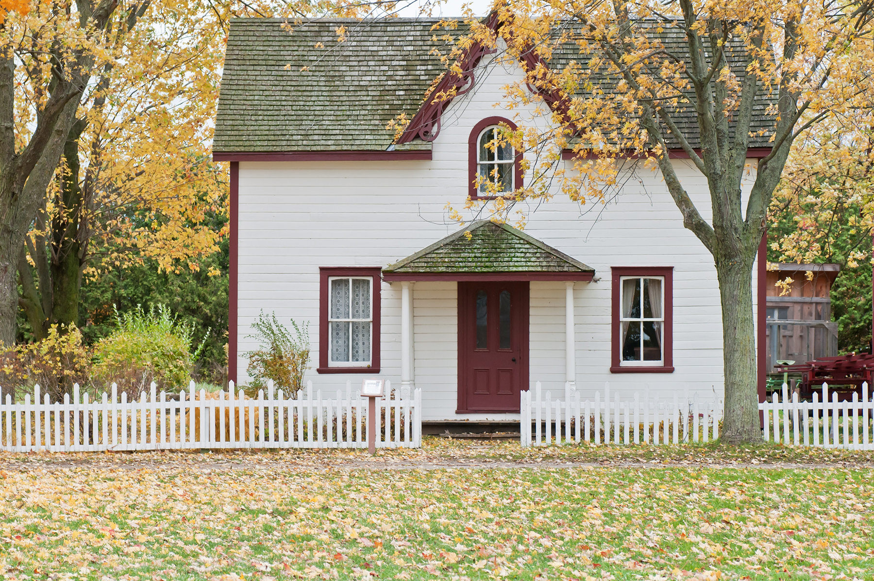 Small white house with red door nestled in woods during autumn